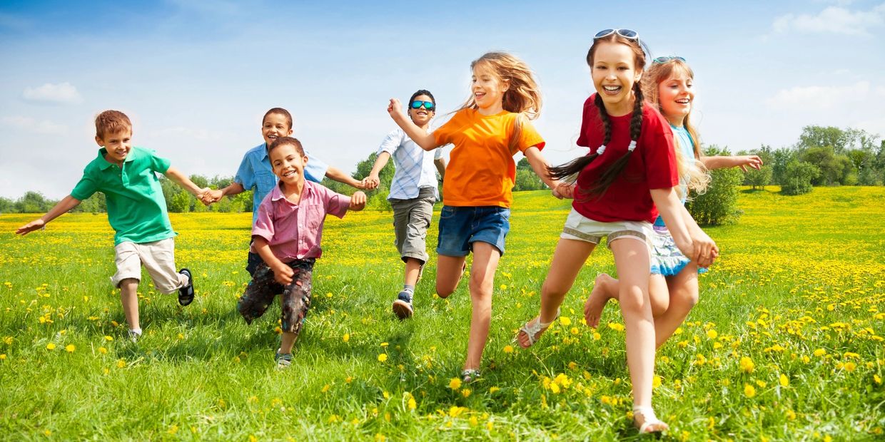Seven young boys and girls hold hands while running through a field during a fitness therapy session
