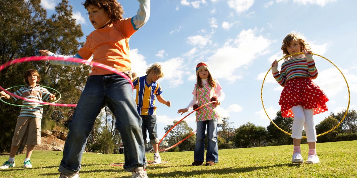 Children participate in a hula-hoop competition at the park during an ABA therapy outing.