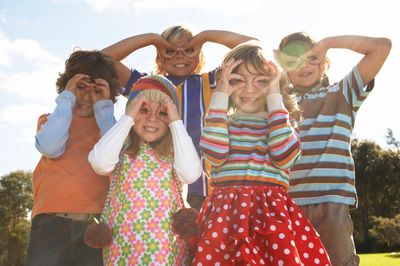 Five children making playful glasses with their hands outdoors.