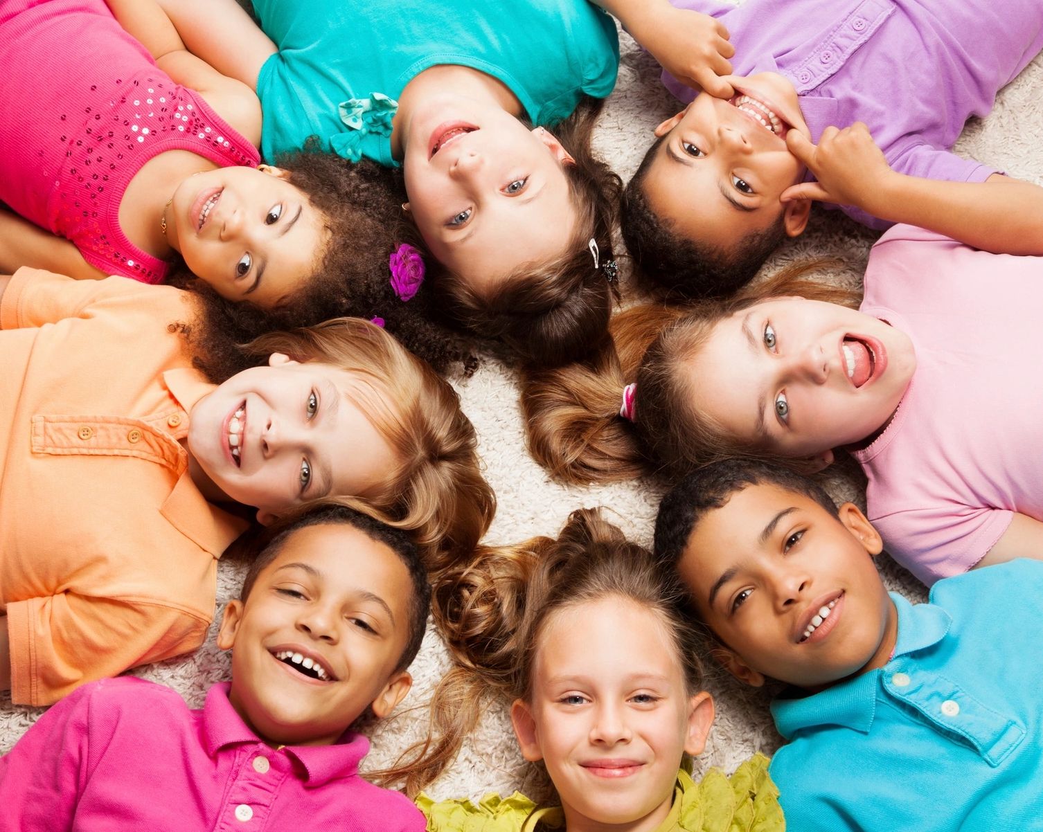 A diverse group of children lying in a circle, smiling and having fun.