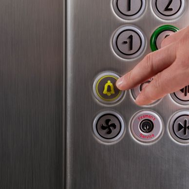 Finger pressing elevator alarm button with bell symbol.