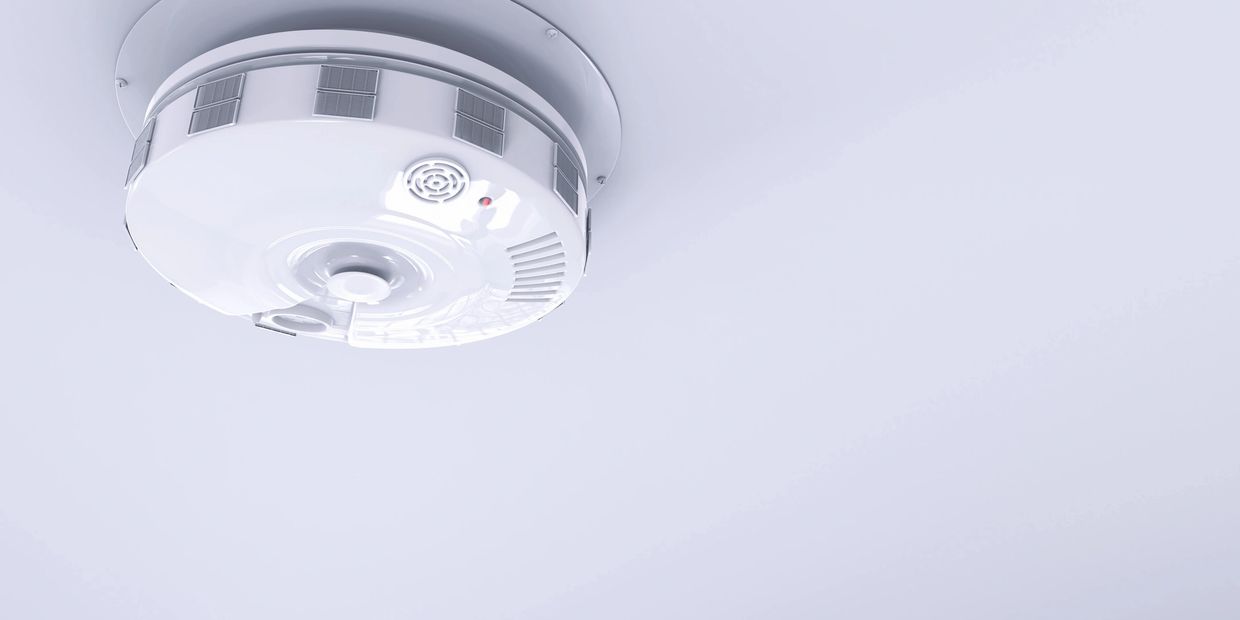 A white smoke detector mounted on a ceiling for fire safety.