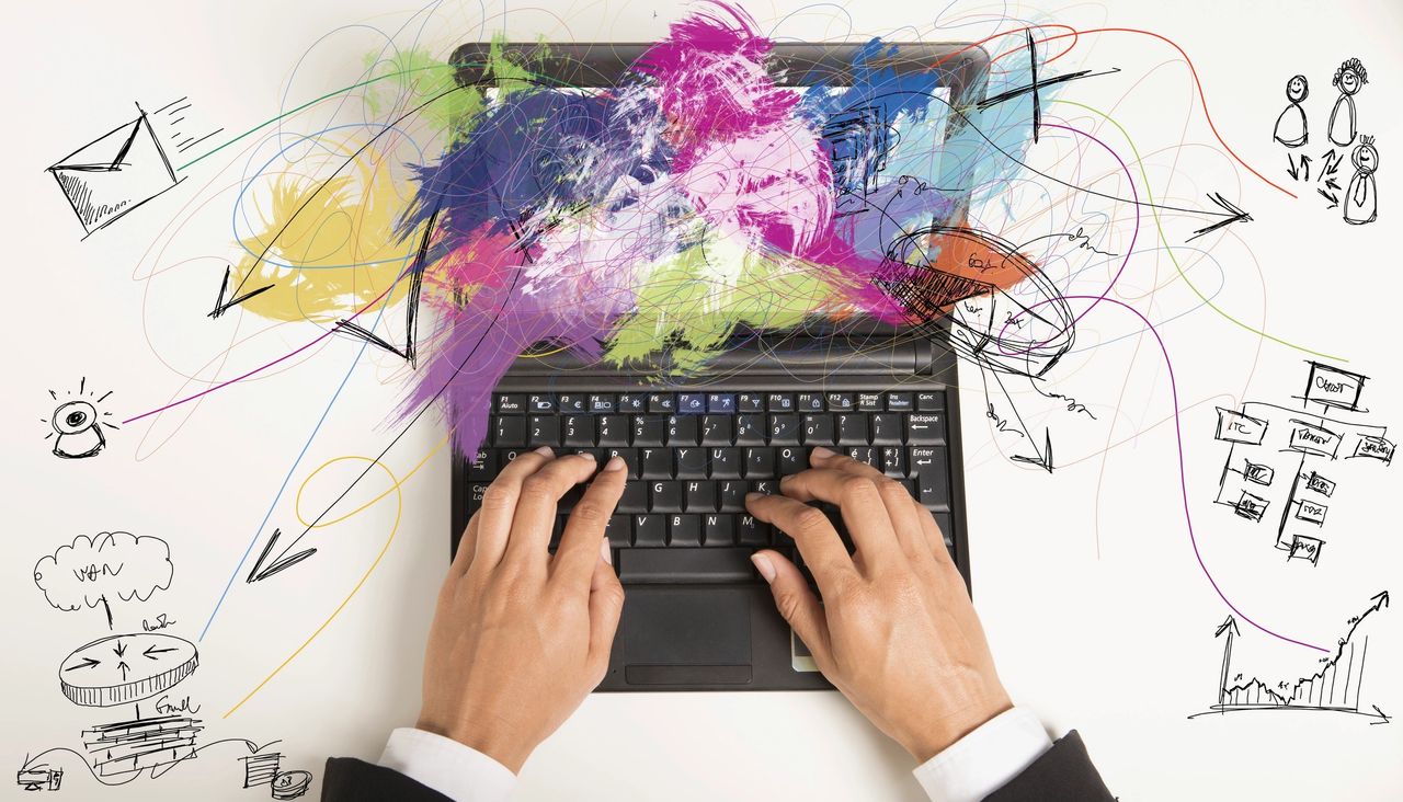 An array of colorful paint and ideas cover a laptop screen, artistically placed, as a person types on a laptop.