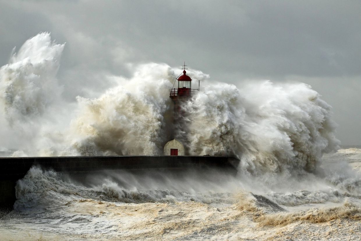 Massive waves crashing against a lighthouse during a stormy day.