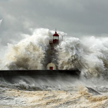 A lighthouse being engulfed by massive ocean waves during a storm.