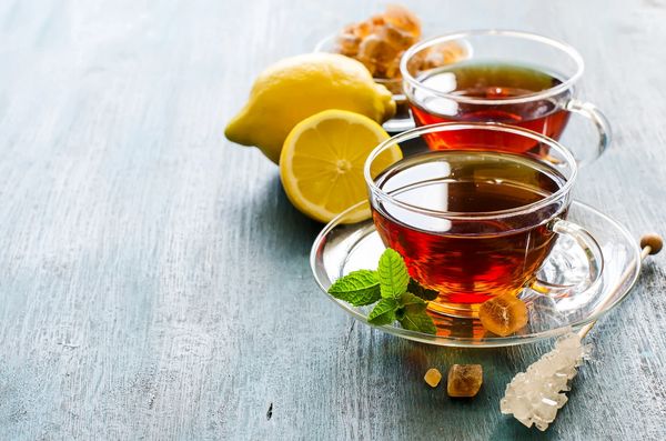 Two glass cups of tea with lemon and rock sugar on a blue wooden surface.