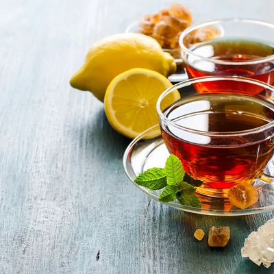Two cups of tea with lemon, ginger, and mint on a wooden surface.