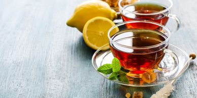 Two cups of tea with lemon and mint on a wooden surface.