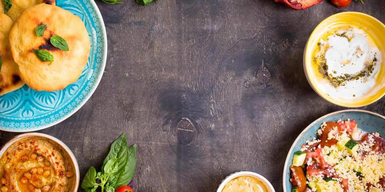 Middle Eastern meal with flatbread, hummus, salad, and fresh herbs on a wooden table.