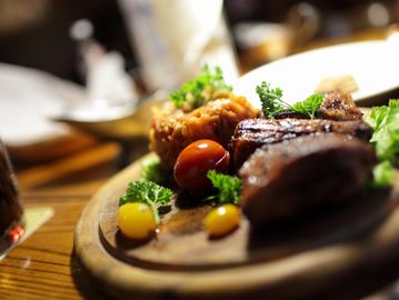 Grilled steak with tomatoes and herbs on a wooden board.