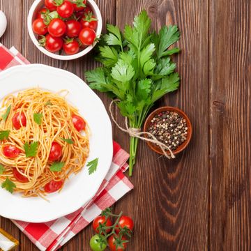 Plate of spaghetti with cherry tomatoes and parsley on a wooden table.