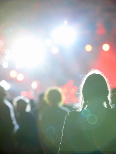 A picture of a concert crowd from ground level behind the crowd looking at blurry lights on stage