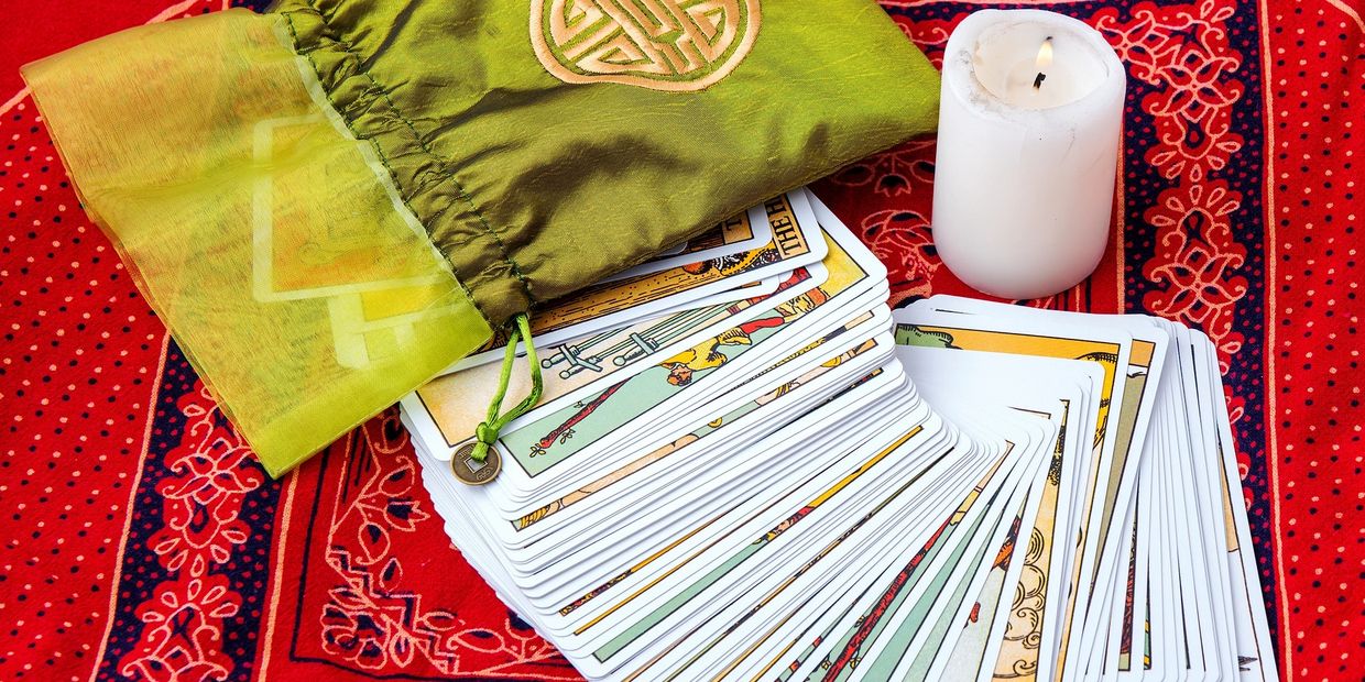 Tarot cards fanned out on a red cloth with a green pouch and burning candle.