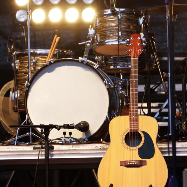 An acoustic guitar and drum set on stage ready for a performance.