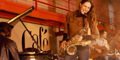 A woman playing saxophone with band at a cafe.