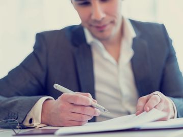 A man in a suit writing on a document with a pen.