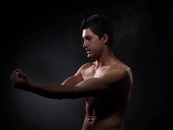 Muscular man stretching his arms against a dark background.