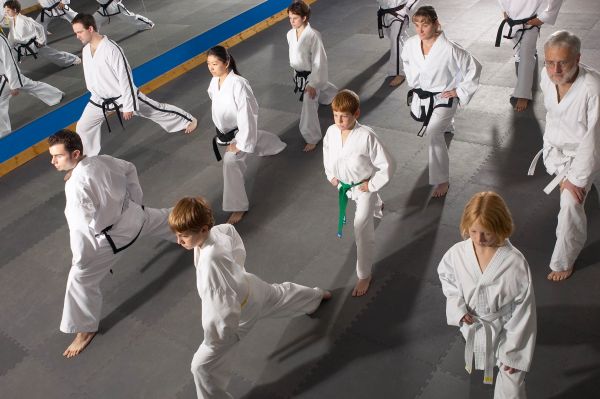 Group practicing martial arts in white uniforms performing kicks.
