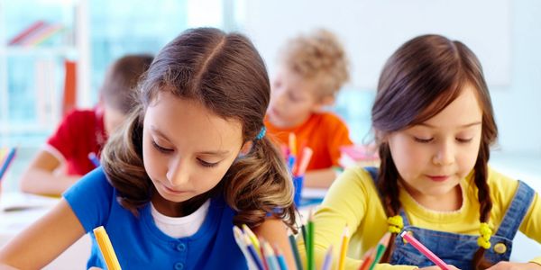 Two girls focused on drawing in a classroom.