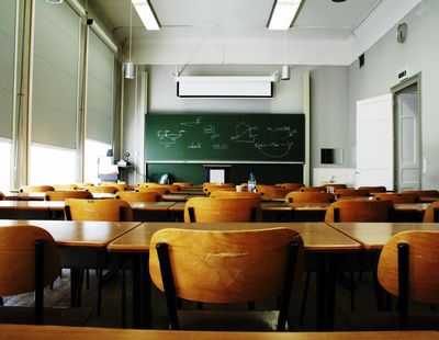 Empty classroom with wooden desks and chalkboard.