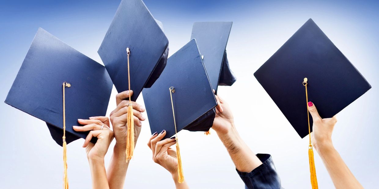 Hands holding up graduation caps against a blue sky background.