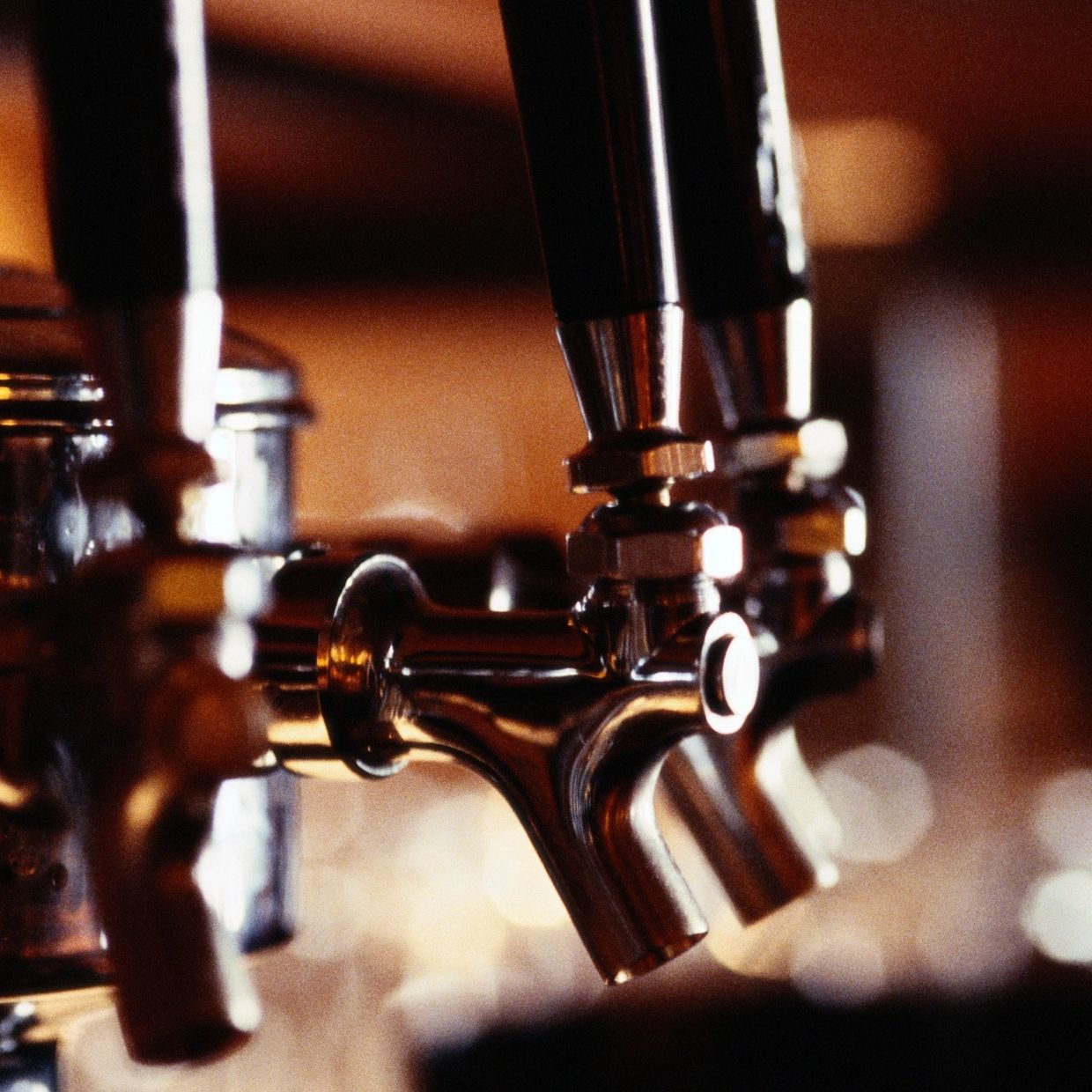Close-up of shiny beer taps in a dimly lit bar.