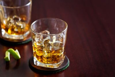 Glass of whiskey with ice on a coaster.