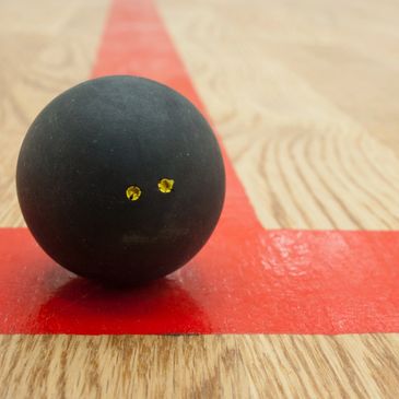 zoomed in picture of a double yellow dot squash ball sat upon the red court lines