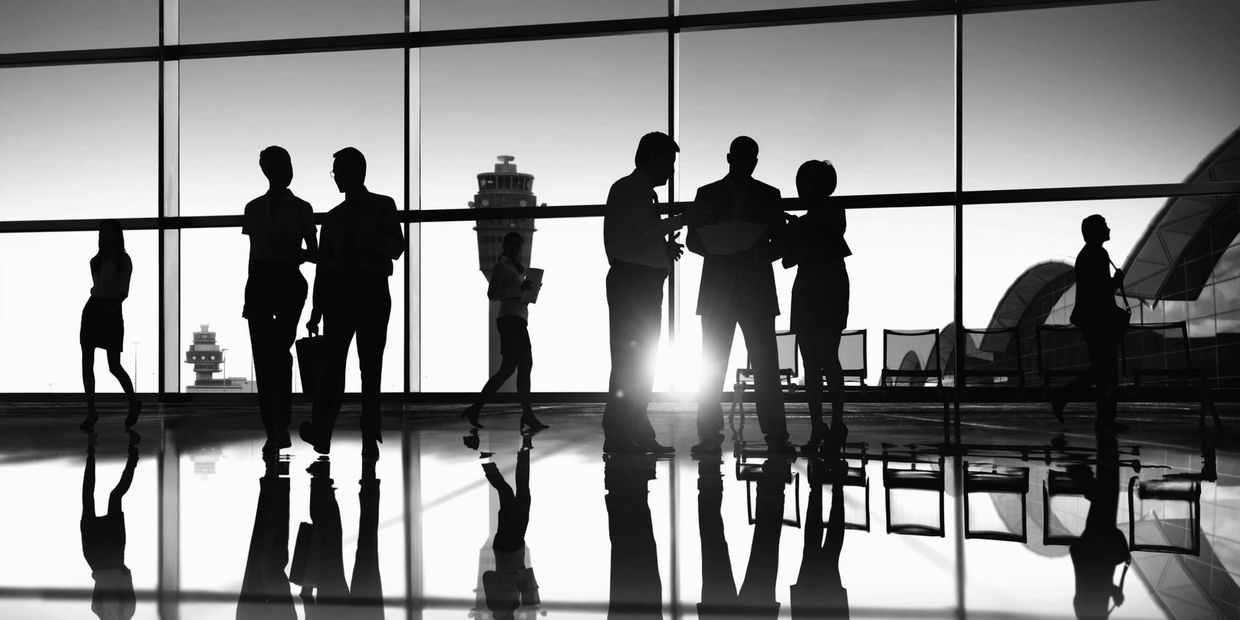 Silhouetted business people converse in a modern airport terminal with reflective floors.