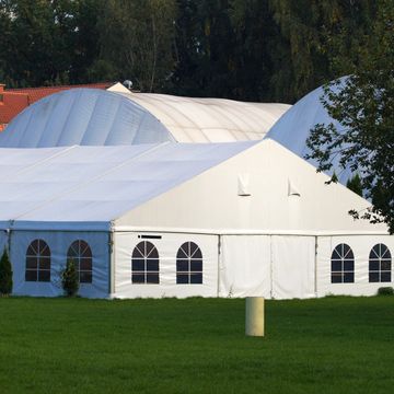Large white event tents set up on green grass under trees.