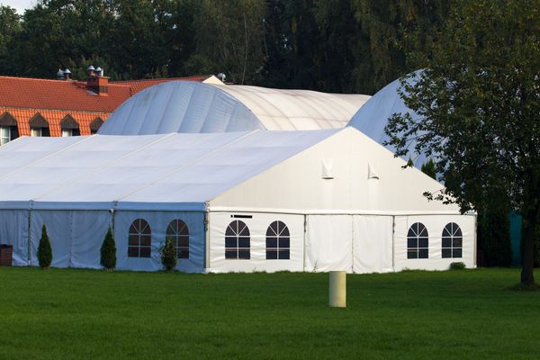 Large white event tents set up on green grass near trees and buildings.