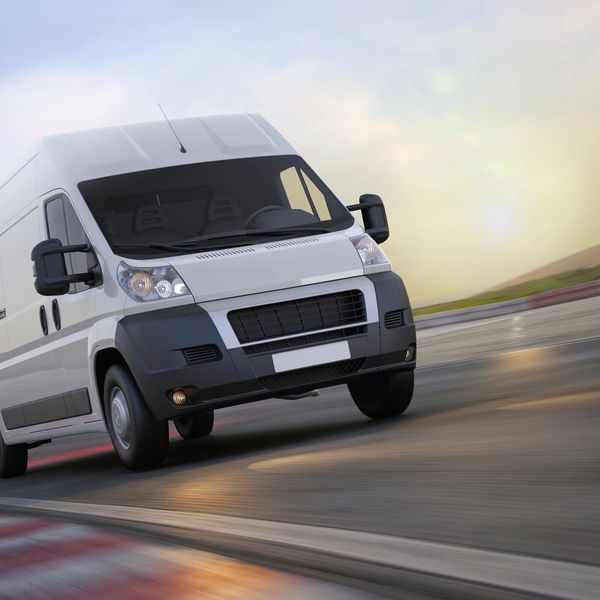 White delivery van speeding on a curved road during sunset.
