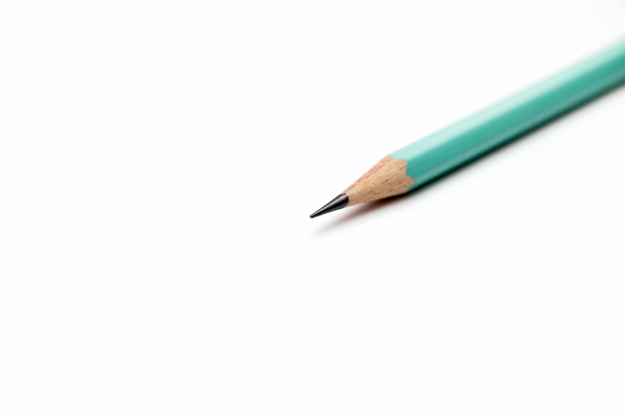 A sharpened teal colored pencil sits on a blank white canvas.