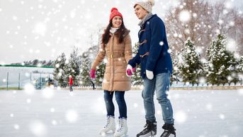A happy couple ice skating outdoors on a snowy winter day.