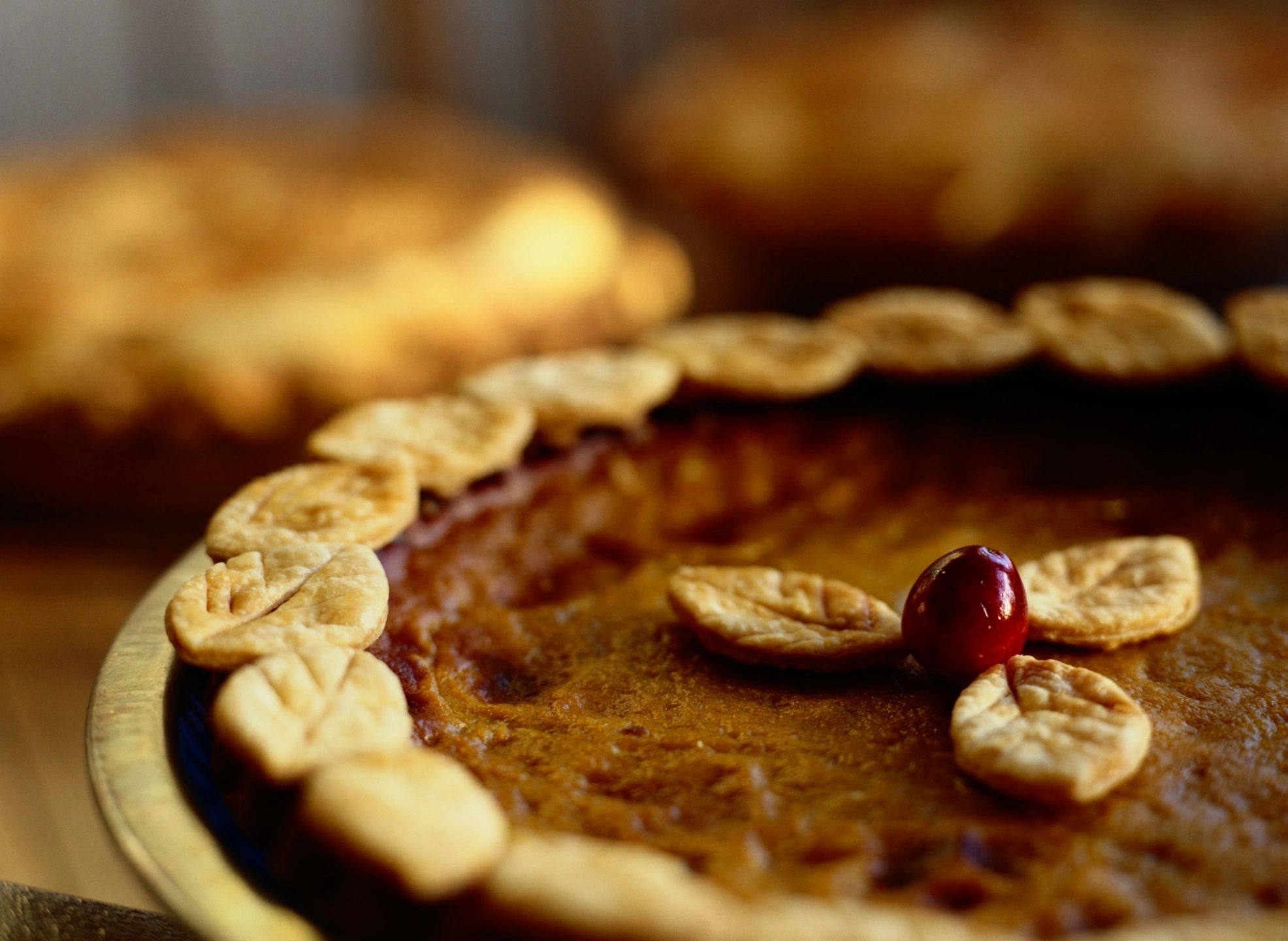 Close-up of a pumpkin pie decorated with leaf-shaped crust and a cherry.