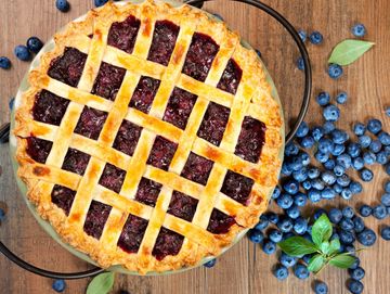 Golden lattice blueberry pie with fresh blueberries on wooden surface.