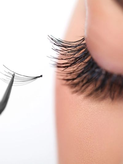 Applying eyelash extensions with tweezers on closed eye.