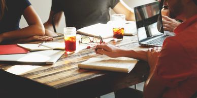 photo of numerous people sitting at a meeting desk covered in laptops, notebooks and soft drinks  