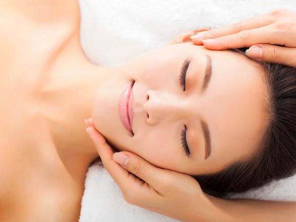 A young woman is getting facial treatment. Two hands are touching the woman's face.