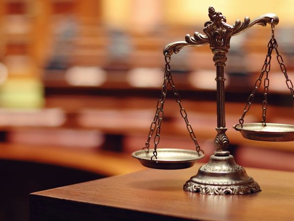 A brass balance scale on a wooden table in a courtroom, by criminal defense attorney Joshua Taylor a