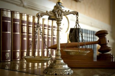 Law books on a bookshelf with the scales of justice and a gavel in the foreground
