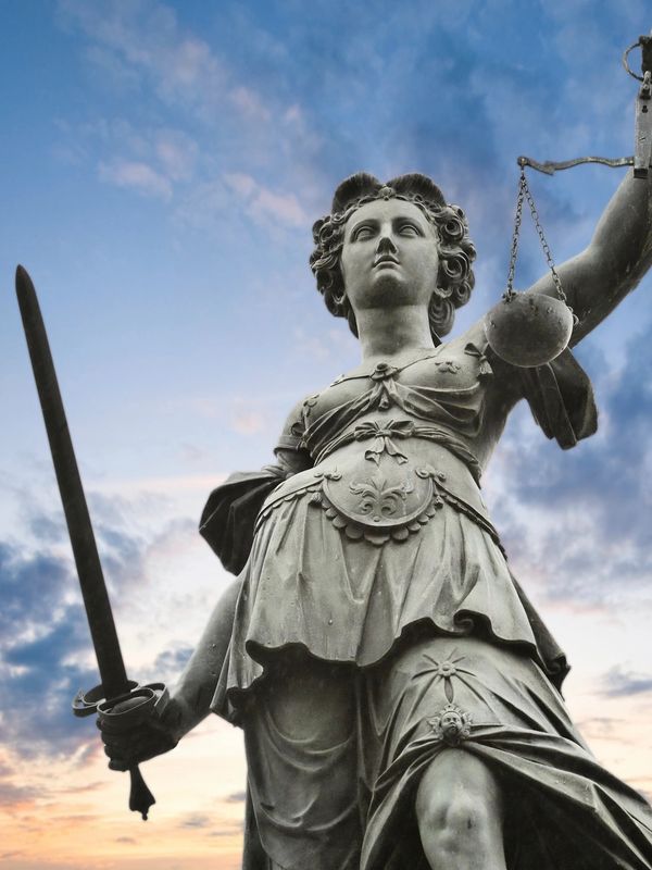 Statue of Lady Justice holding scales and sword against a cloudy sky.