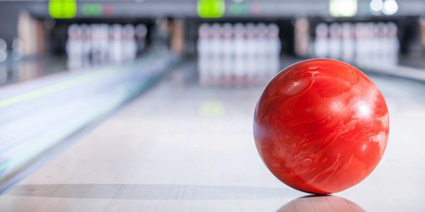 A red bowling ball on a lane with pins in the background.