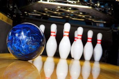A blue bowling ball rolling towards pins in a bowling alley.