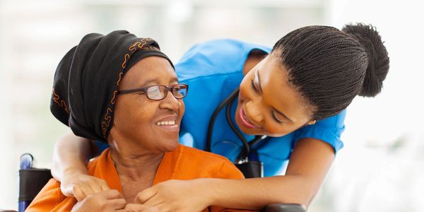 A nurse warmly embraces an elderly woman in a wheelchair, sharing a smile.