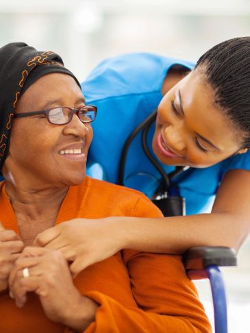 Nurse smiling with elderly patient in wheelchair.