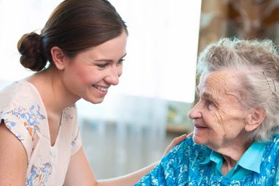 Young woman smiling warmly at an elderly woman in a blue sweater.
