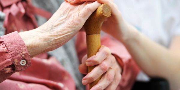 Hands on a cane; an elderly woman with younger female hands comforting
