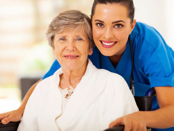 A smiling nurse with an elderly woman in a wheelchair, showing care and support.