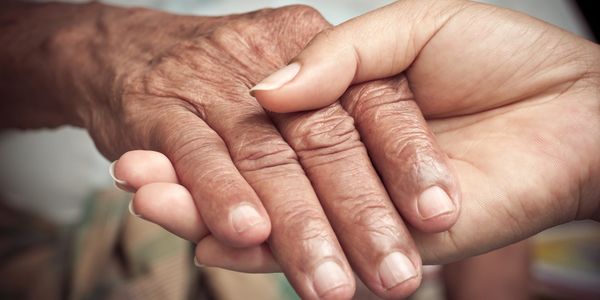 Caregiver's hand holding a elderly gentleman's hand.